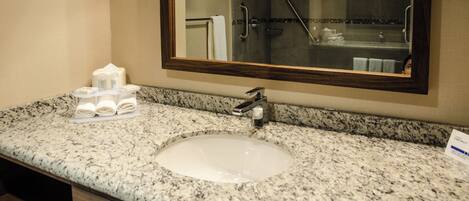 A bathroom with a granite countertop, a sink, a mirror, and a shower stall.