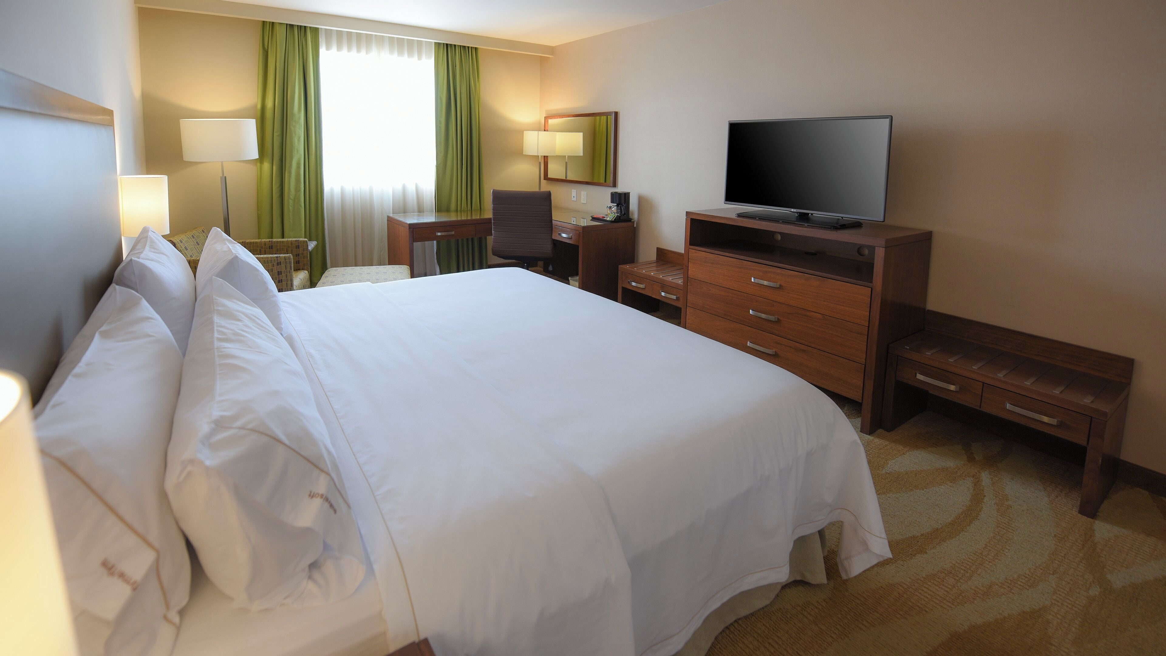 Ett hotellrum med en stor säng, ett skrivbord med en stol, en tv och ett litet bord.