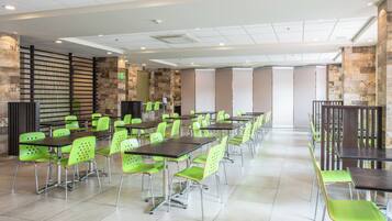 A spacious dining area with high tables and green chairs, a stone accent wall, and a ceiling with recessed lighting.