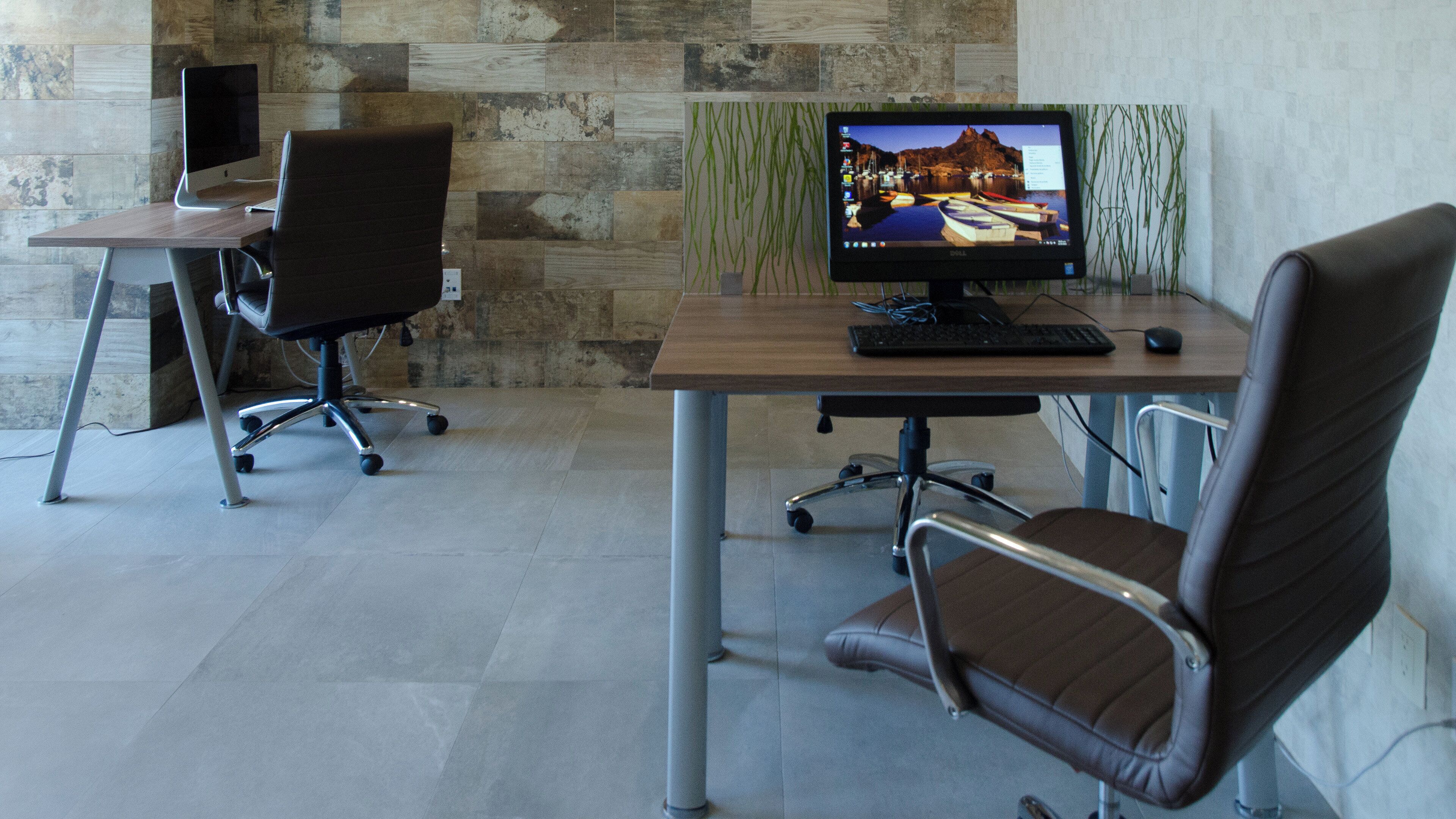 A modern office space with a desk, two chairs, a computer monitor, and a keyboard.