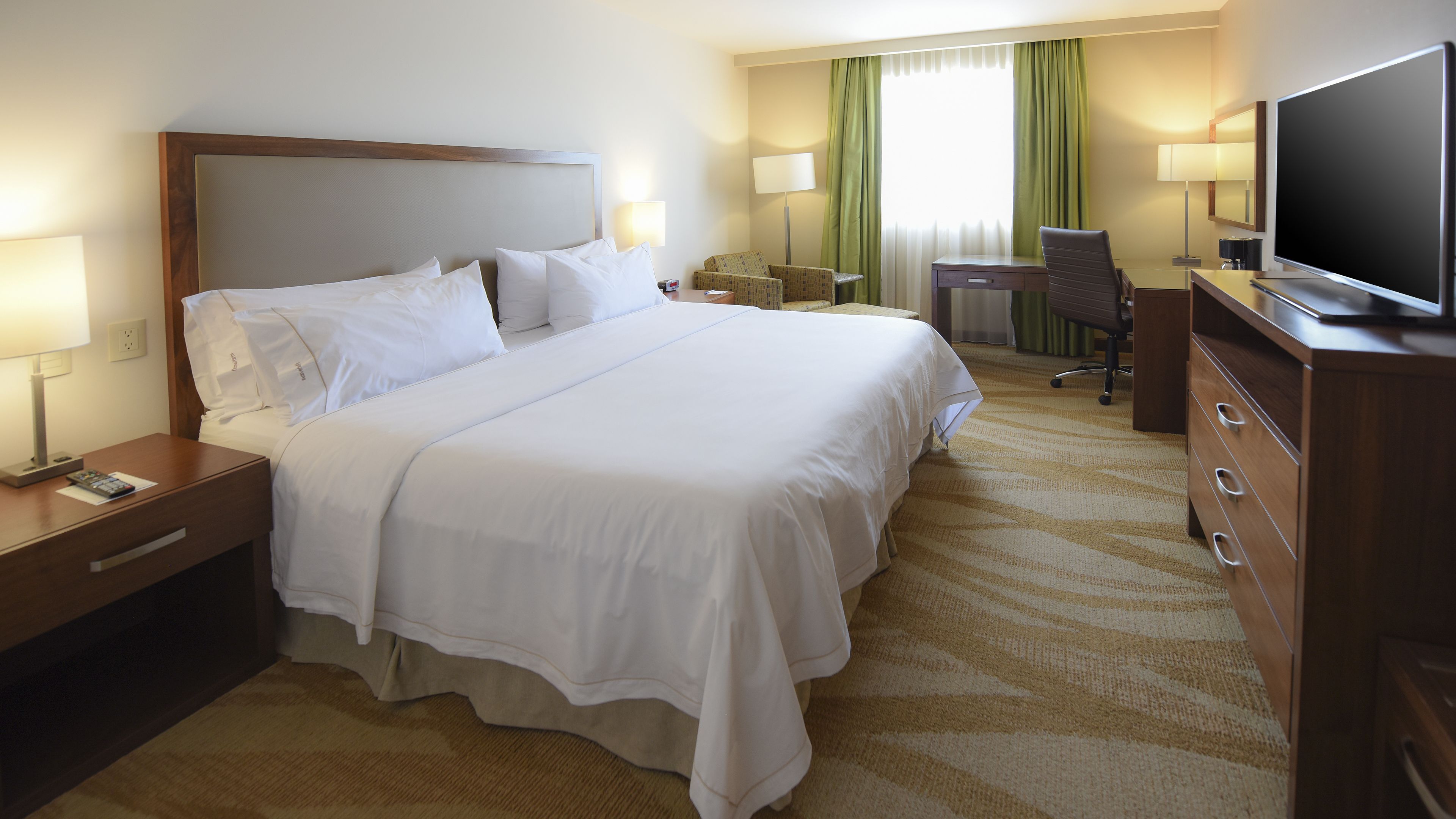 Une chambre d’hôtel avec un grand lit, un bureau, une chaise, une télévision et une commode.