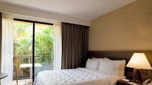A hotel room with a bed, a nightstand with a lamp, a small table, and a balcony with a view of greenery. - Holiday Inn Express & Suites Celaya by IHG (Celaya)