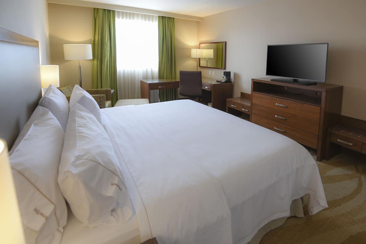 A hotel room with a large bed, a desk with a chair, a television, and a small table.