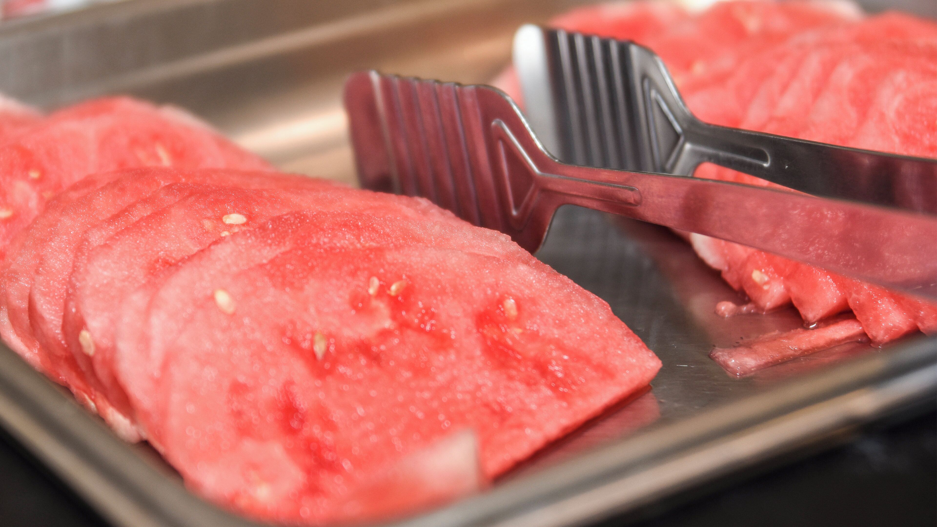 A tray with sliced watermelon and a black spatula.