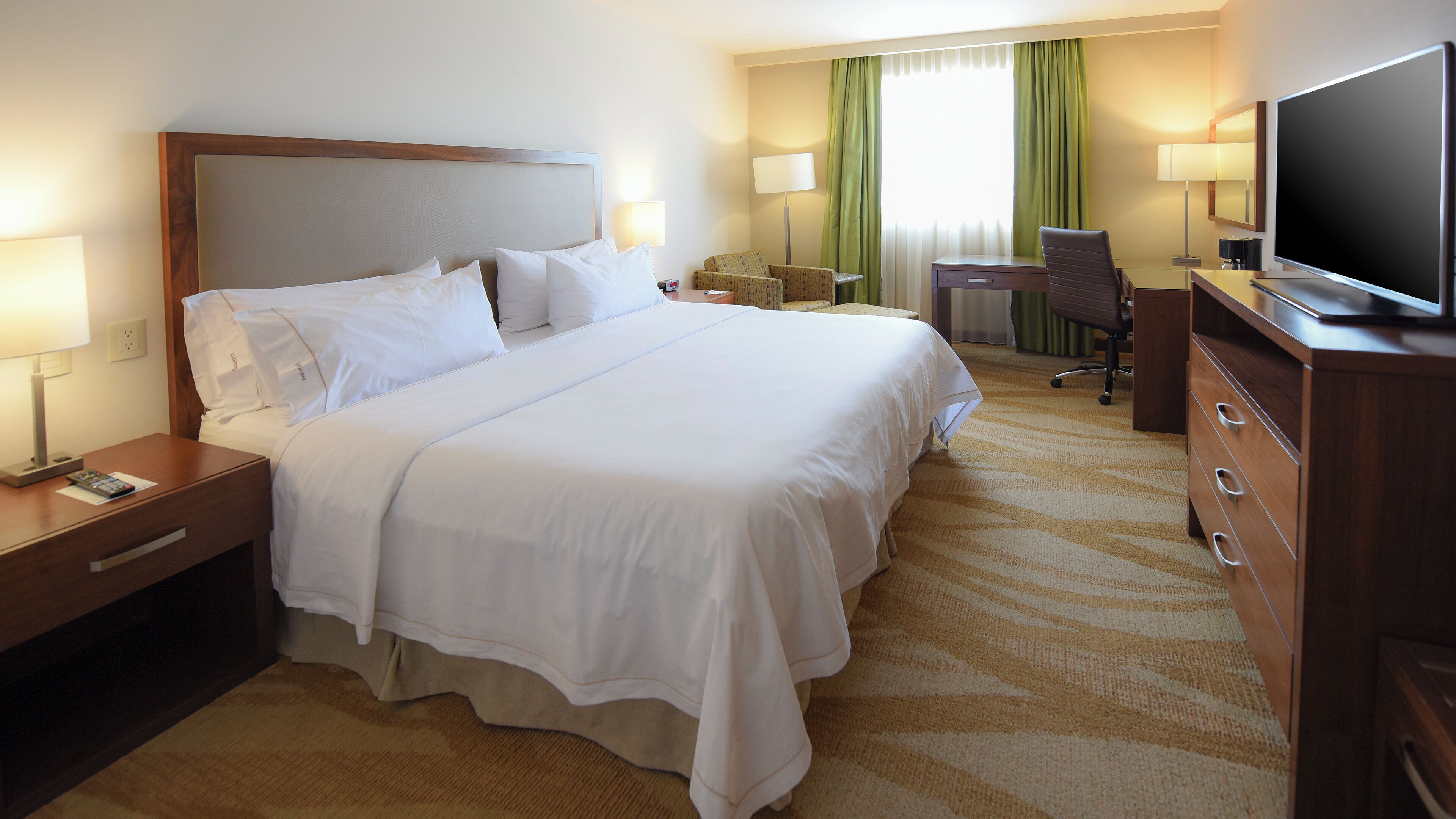 A hotel room with a large bed, a desk, a chair, a television, and a lamp.