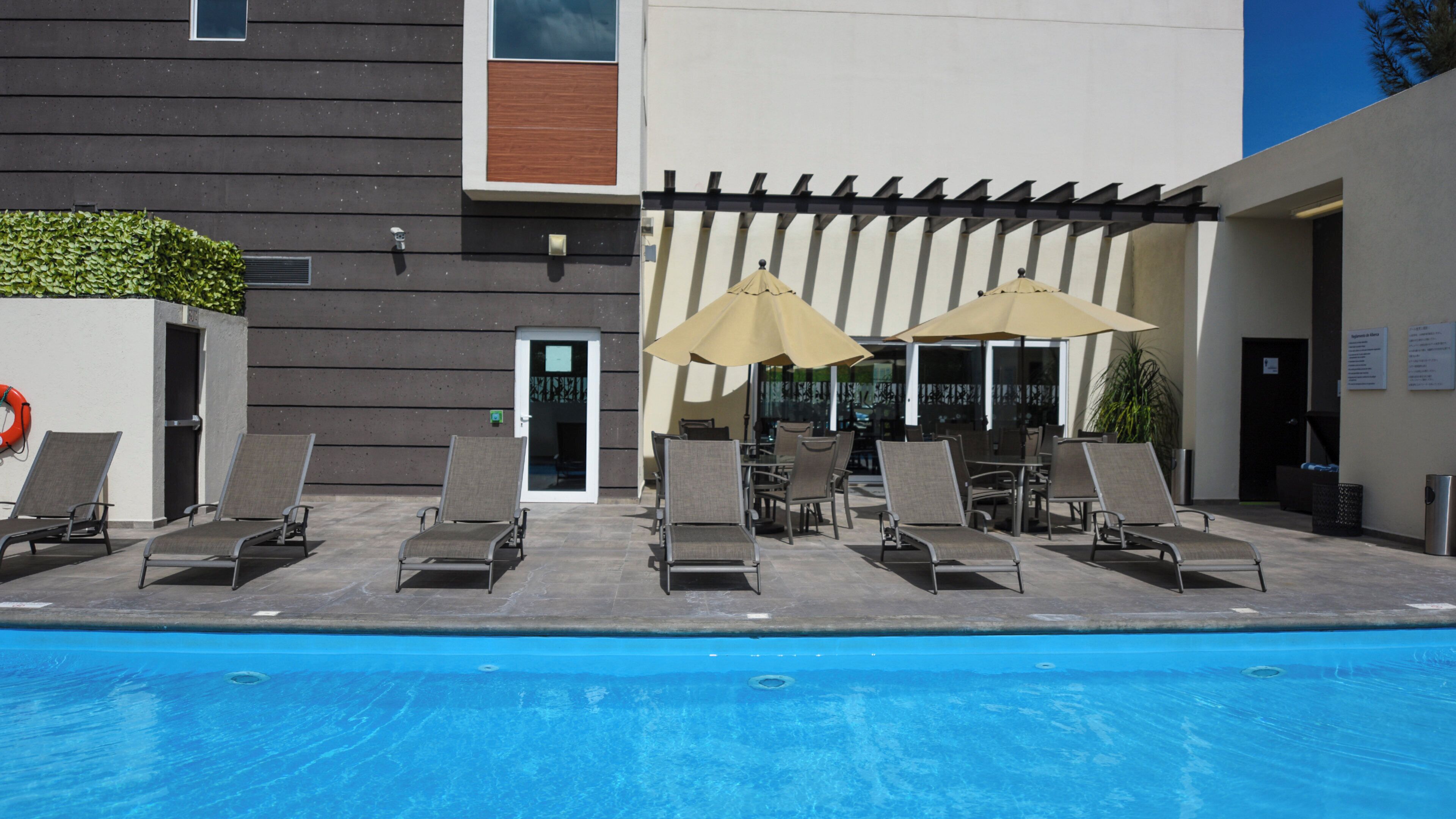 Una zona junto a la piscina con sillones reclinables y sombrillas, una puerta y una pared con ventana.