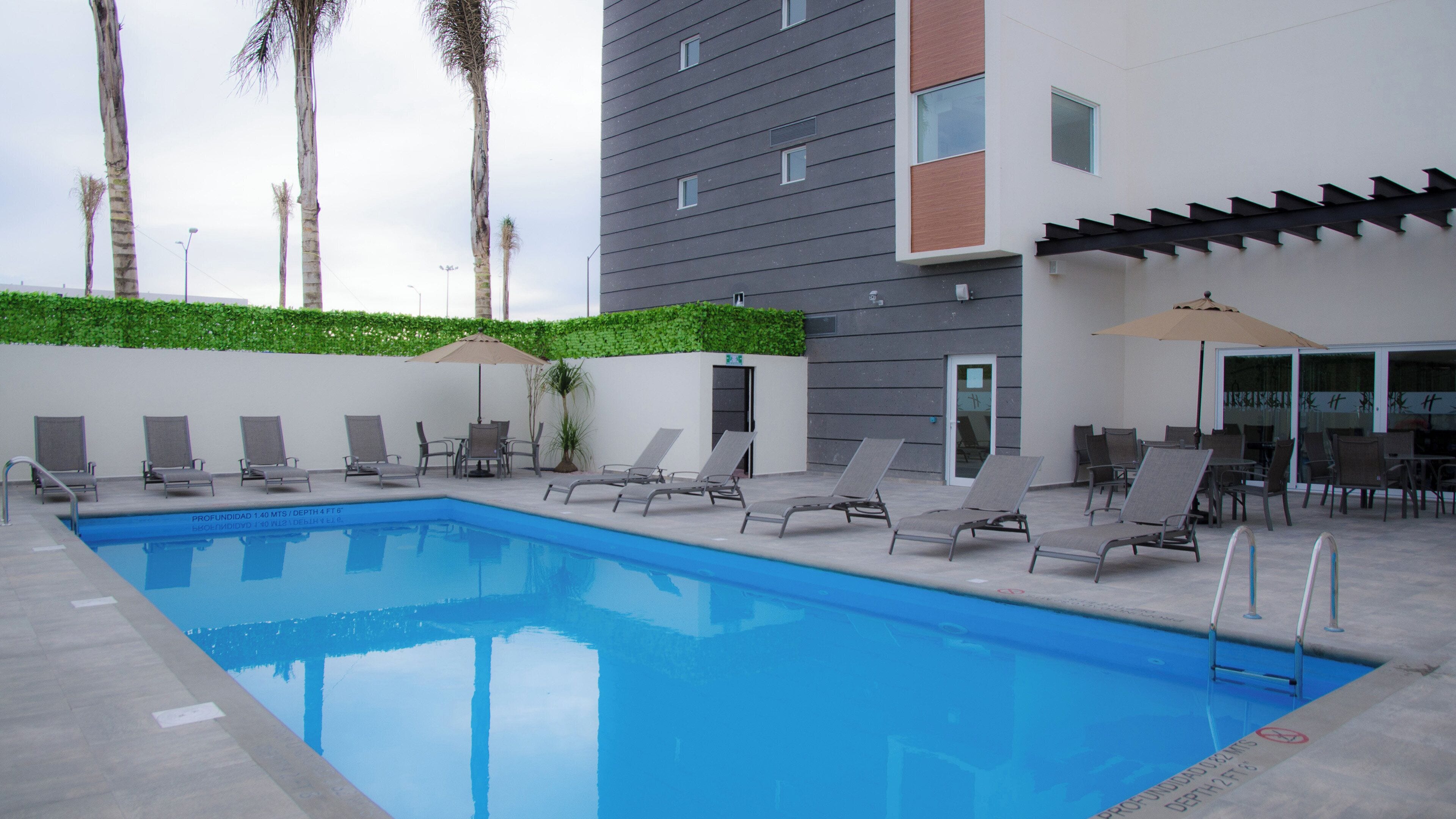 Una piscina con sillones de descanso y sombrillas, rodeada por un edificio de diseño moderno.