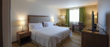 A hotel room with a large bed, bedside tables, a desk, a chair, and a television.