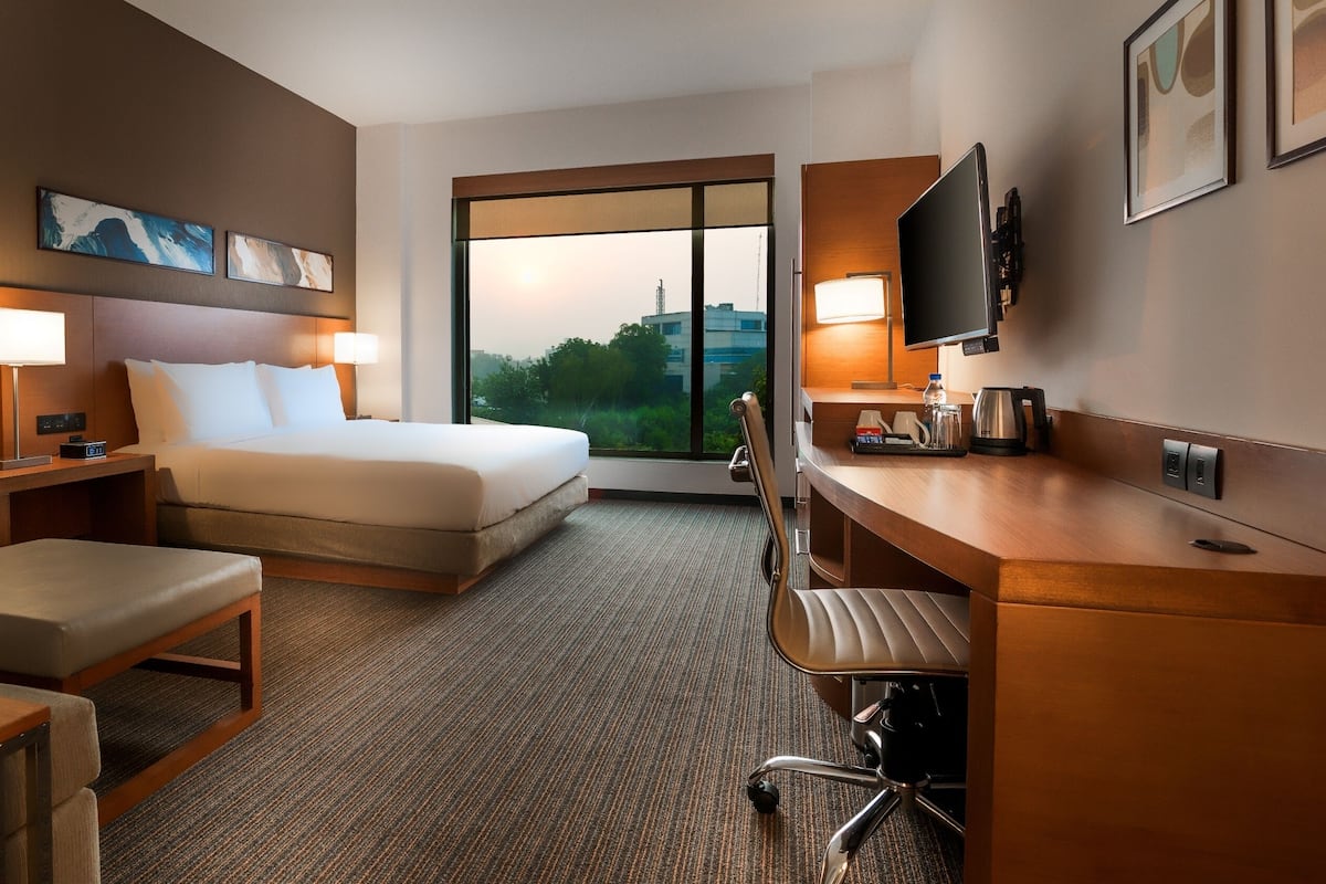 A hotel room with a bed, a desk, a chair, a TV, and artwork on the wall.
