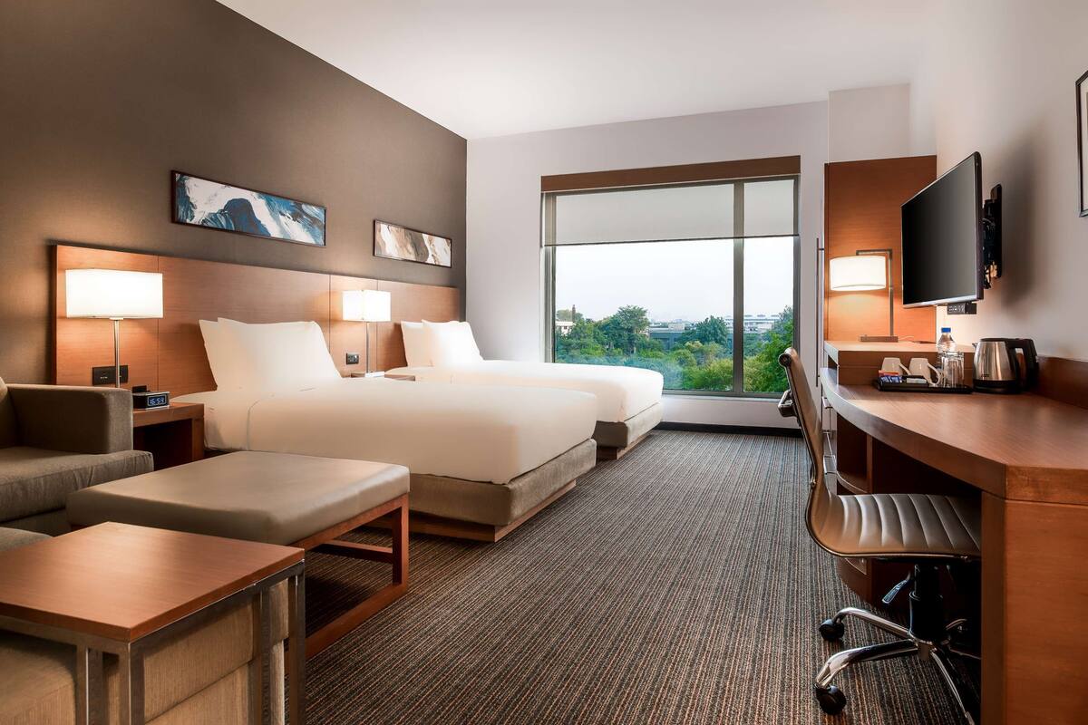 A hotel room with a bed, a desk, a chair, a sofa, and a TV.