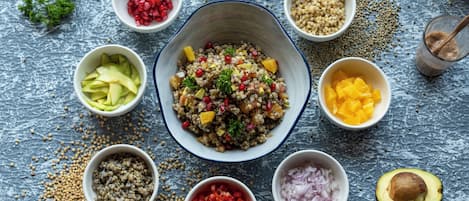 A bowl of salad with various ingredients and surrounding bowls of fruits and vegetables.
