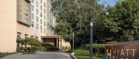 A modern hotel entrance with a sign reading "HYATT PLACE," surrounded by well-maintained greenery and a clear sky.