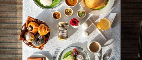 A table set with various dishes including bread, soup, and fruits, along with a rose and a glass of juice.