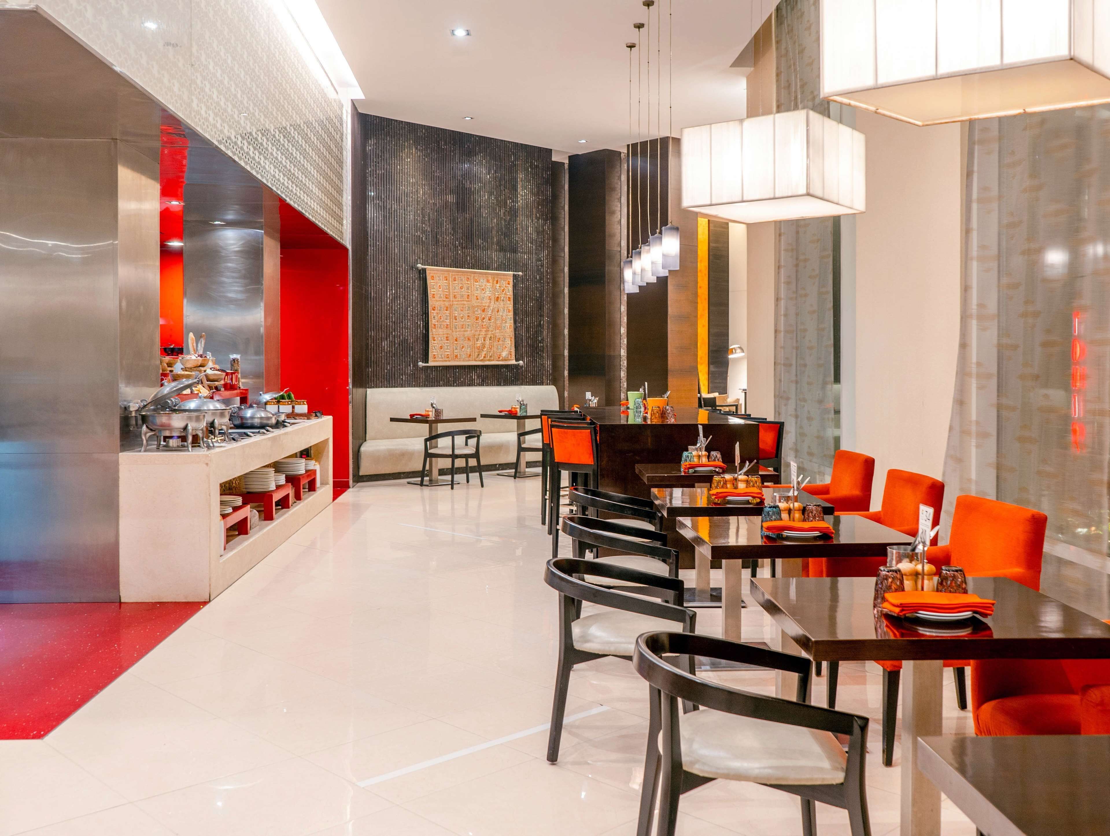 A modern dining area with multiple tables and chairs, a buffet setup on the left, and a large abstract painting on the wall.