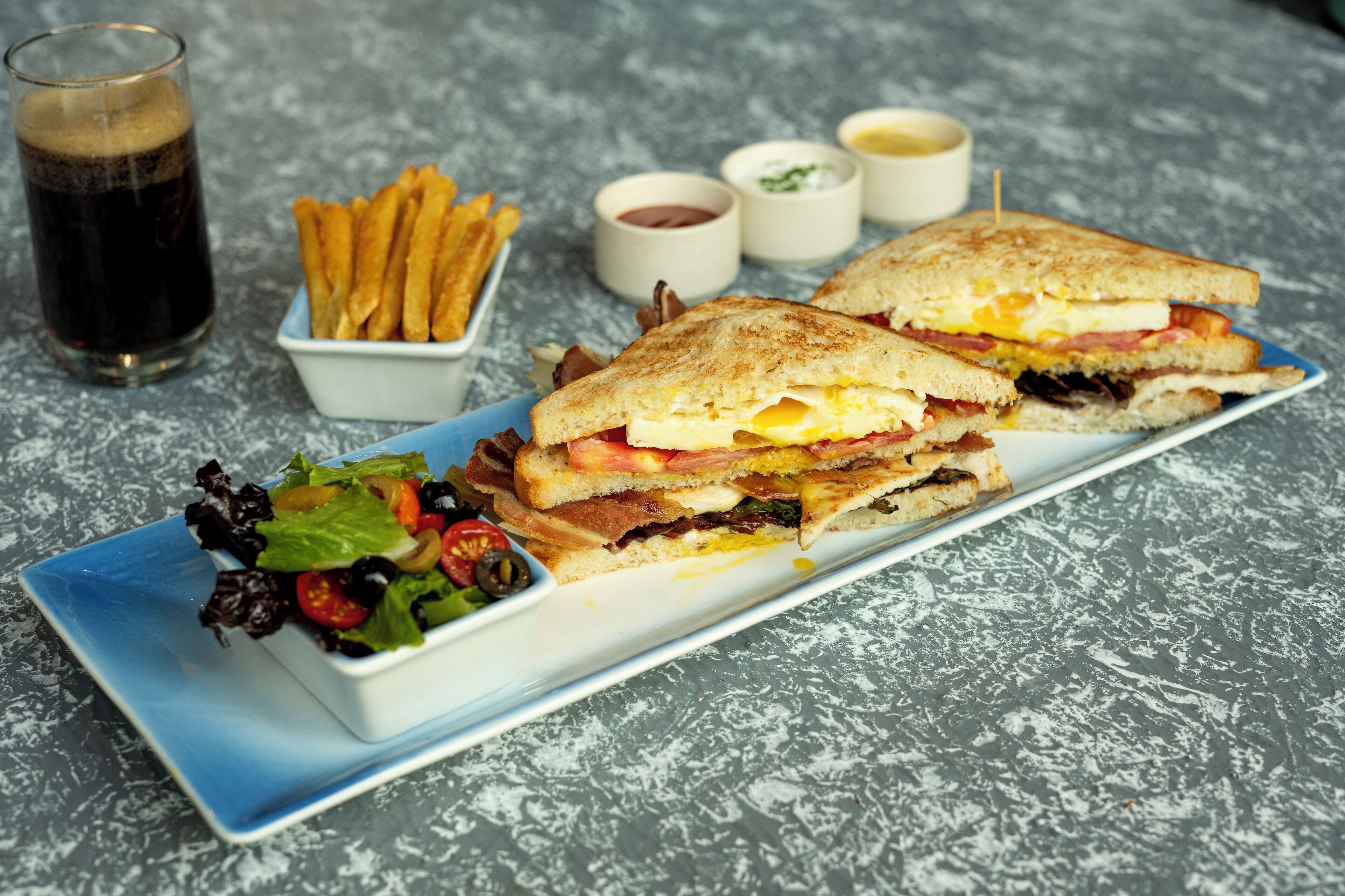 Un sandwich servi sur une assiette, accompagné de frites et d’une boisson.