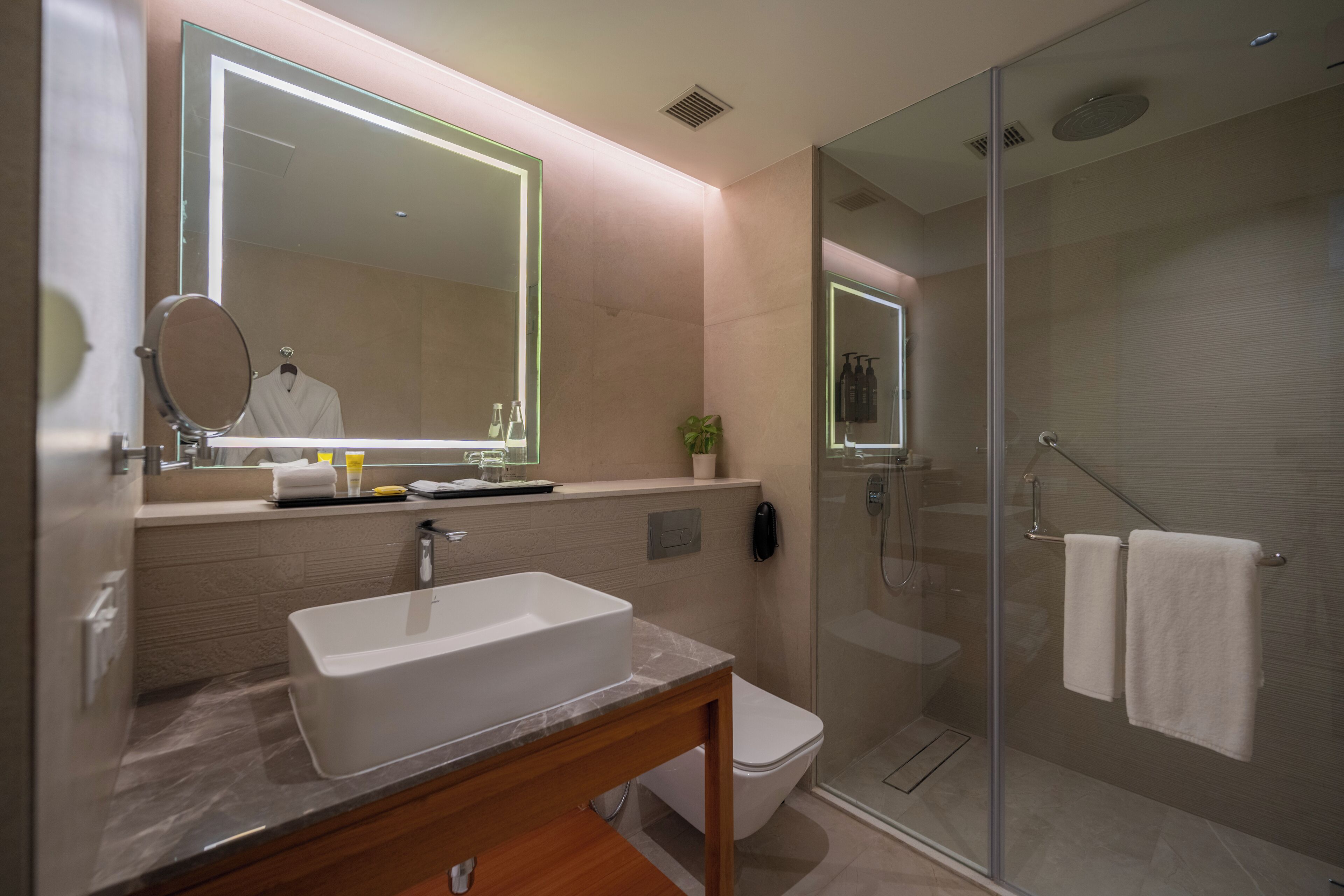 Un baño moderno con un espejo grande, un lavabo, un inodoro y una ducha con mampara de vidrio.
