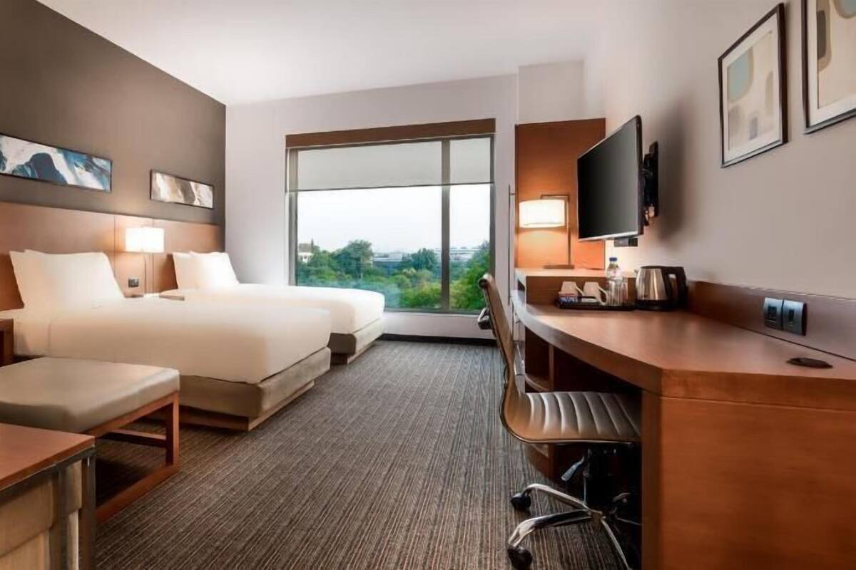 A hotel room with a bed, two bedside tables, a desk, a chair, a TV, and a window with a view.