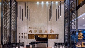Un magnifique piano à queue trône dans un vaste hall d’entrée orné d’un mur de marbre et de panneaux décoratifs.