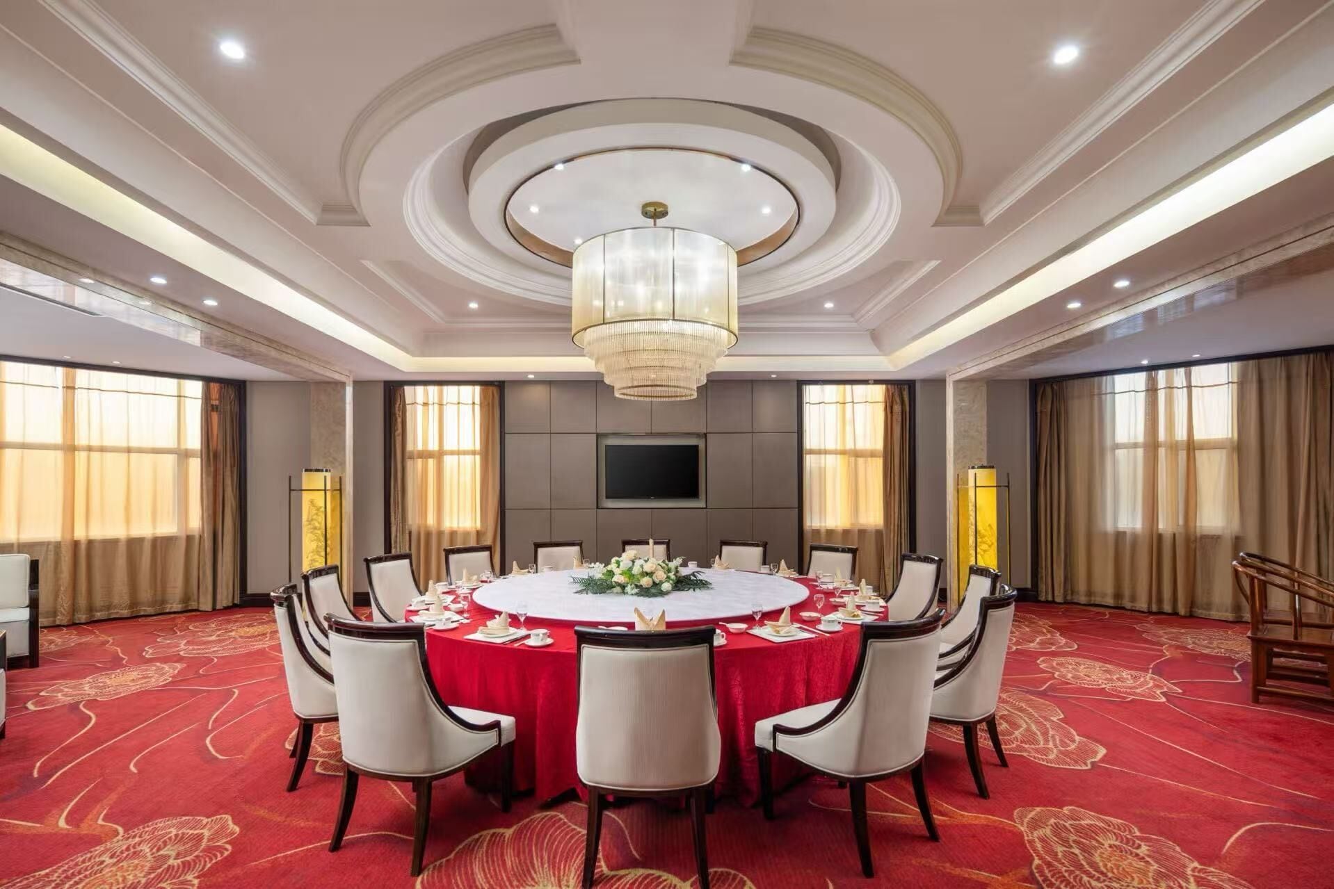 A conference room with a round table, white chairs, and a red tablecloth.