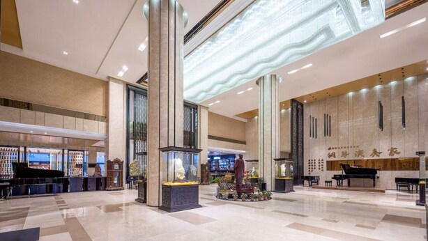 Un hall d’entrée spacieux avec de hauts plafonds, un grand piano, une statue et un coin bar.