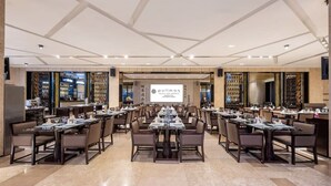 Une grande salle de conférence avec de nombreuses tables dressées pour le repas, un grand écran affichant le nom de l’hôtel et un meuble à vin en arrière-plan.