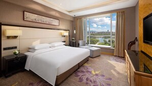 Une chambre d’hôtel avec un grand lit, des tables de chevet, une télévision et une vue sur le paysage urbain grâce à de grandes fenêtres.