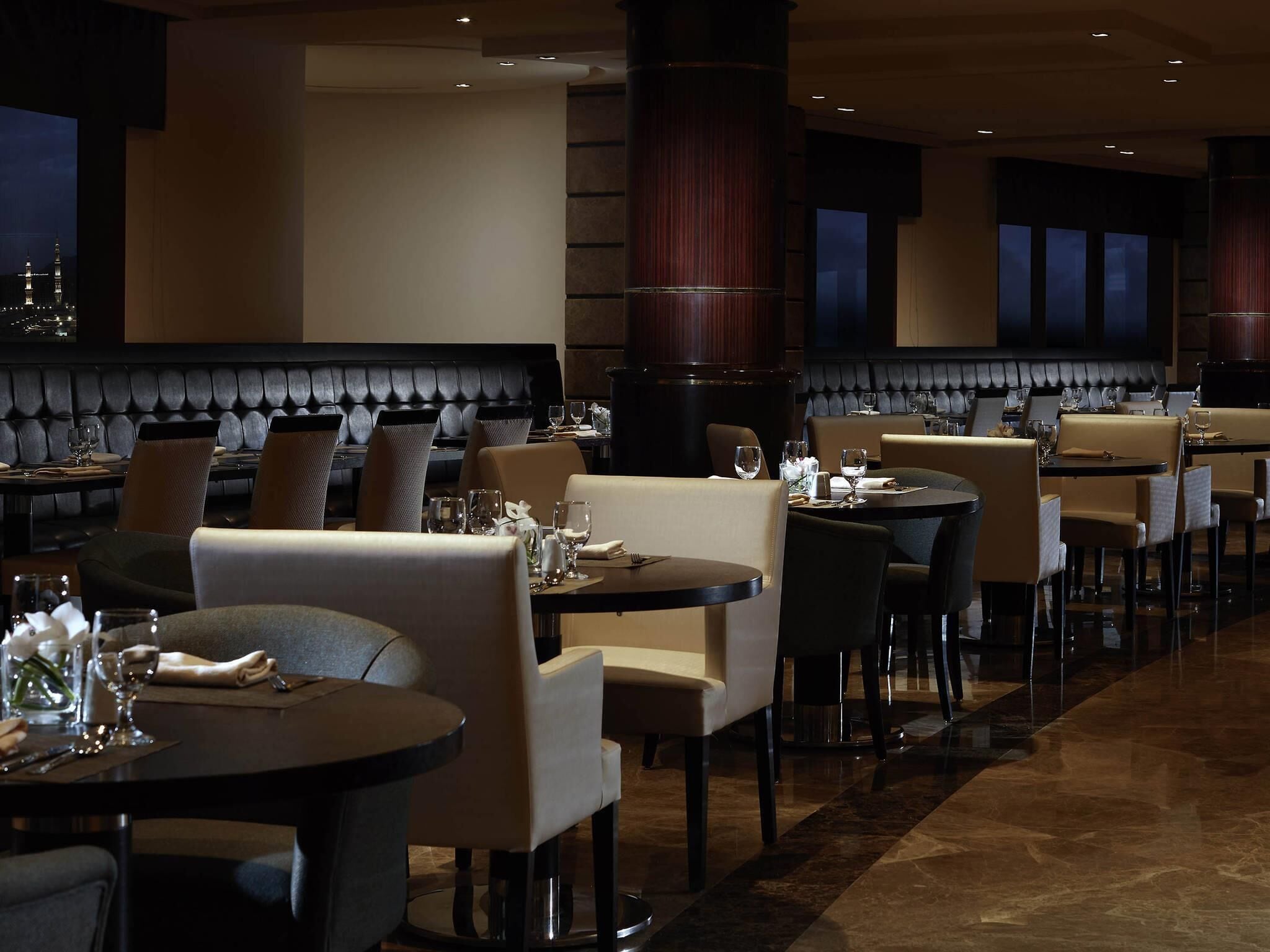 A restaurant with leather booths, round tables, and a view of city lights.