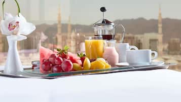 A breakfast tray with fruits, juices, and a coffee pot, set against a cityscape with minarets.