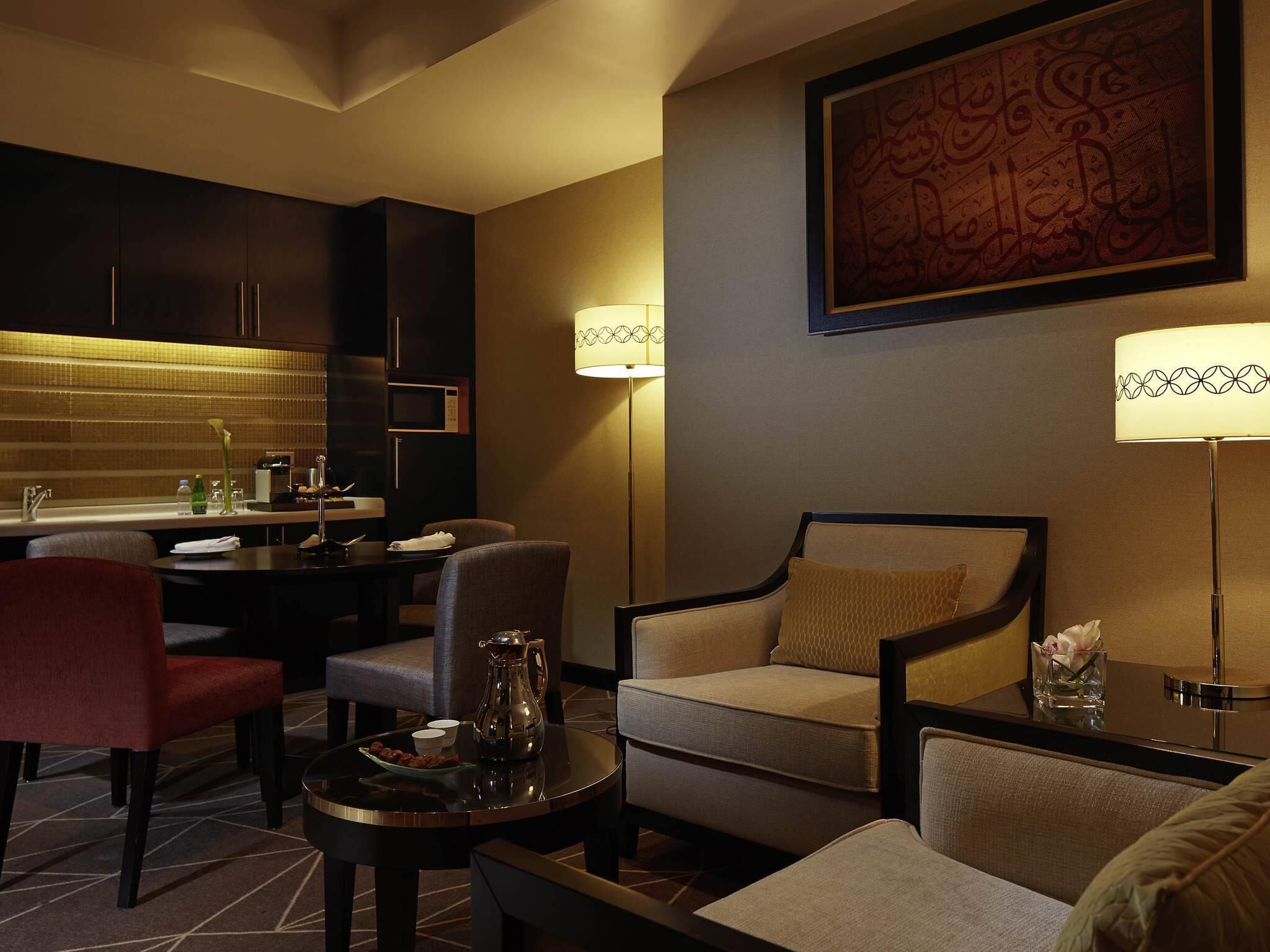 A hotel room with a dining area, a sofa set, a coffee table, and a wall-mounted artwork.