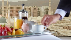 A breakfast setting with a coffee pot, cup, and fruit on a tray, with a view of a mosque and mountains in the background.