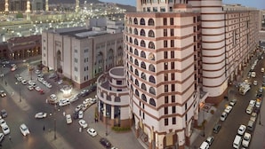 A multi-story building with a central courtyard, surrounded by a busy urban street with cars and a mosque in the background.