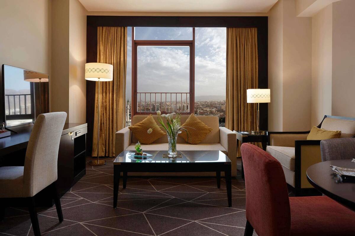 A hotel room with a sofa, a coffee table, a TV, and a view of the city.