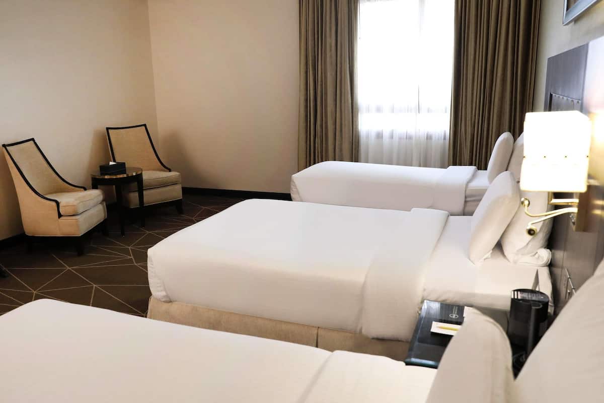 A hotel room with two beds, a chair, a small table, and a lamp.