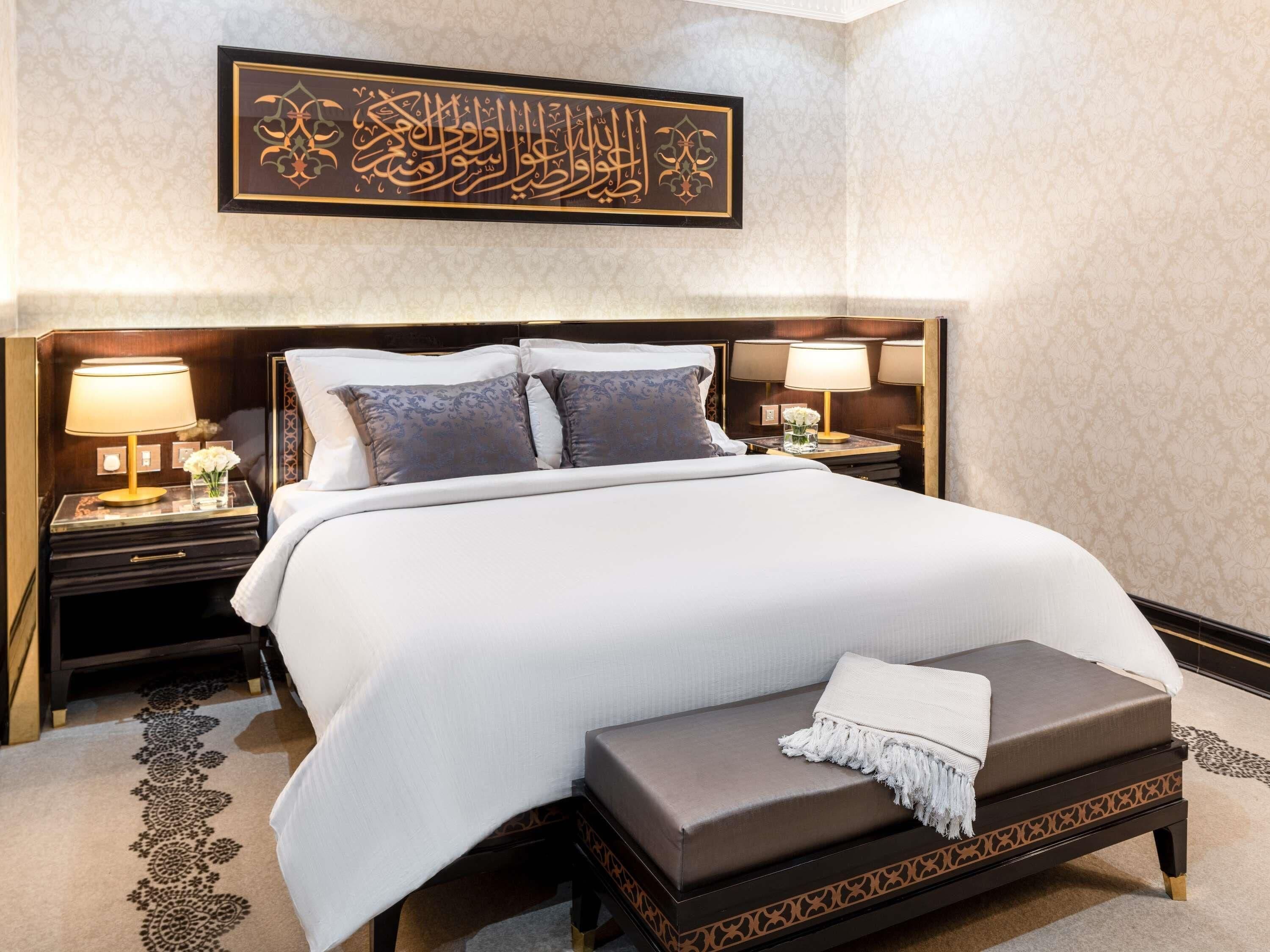 A hotel room with a large bed, two bedside tables with lamps, a decorative wall hanging, and a patterned carpet.
