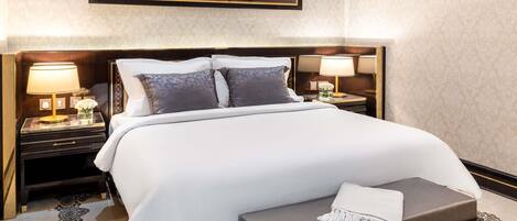 A hotel room with a large bed, two bedside tables with lamps, a decorative wall hanging, and a patterned carpet.