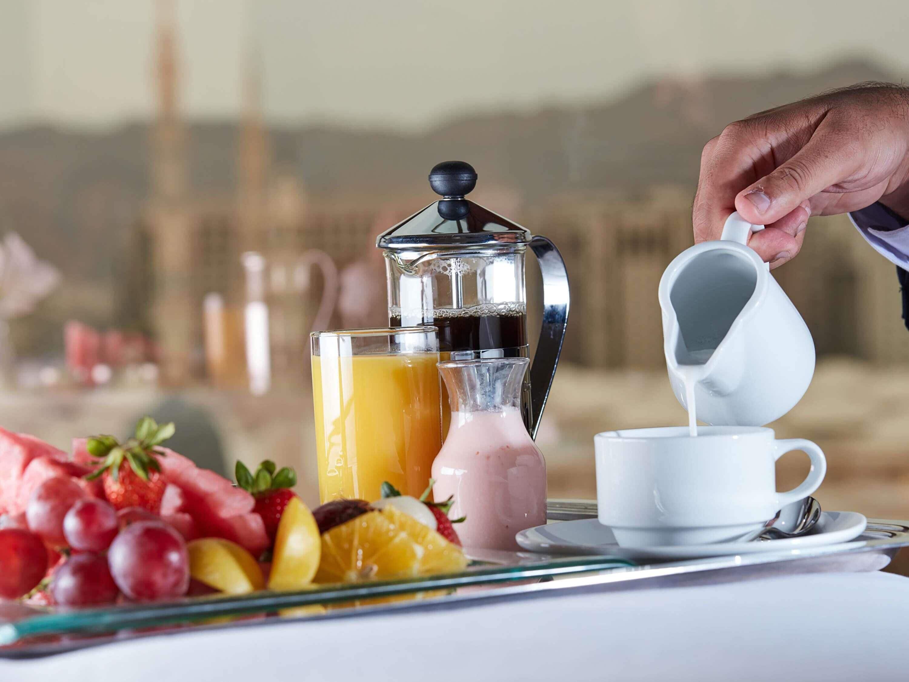 A breakfast setting with a coffee maker, a glass of orange juice, a pitcher of pink beverage, and a plate of fruit.