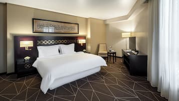 A hotel room with a large bed, a desk, a chair, a TV, and a framed artwork on the wall.