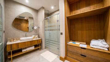 Un baño moderno con tocador de madera, un espejo grande, cabina de ducha de vidrio y un estante de madera con toallas.