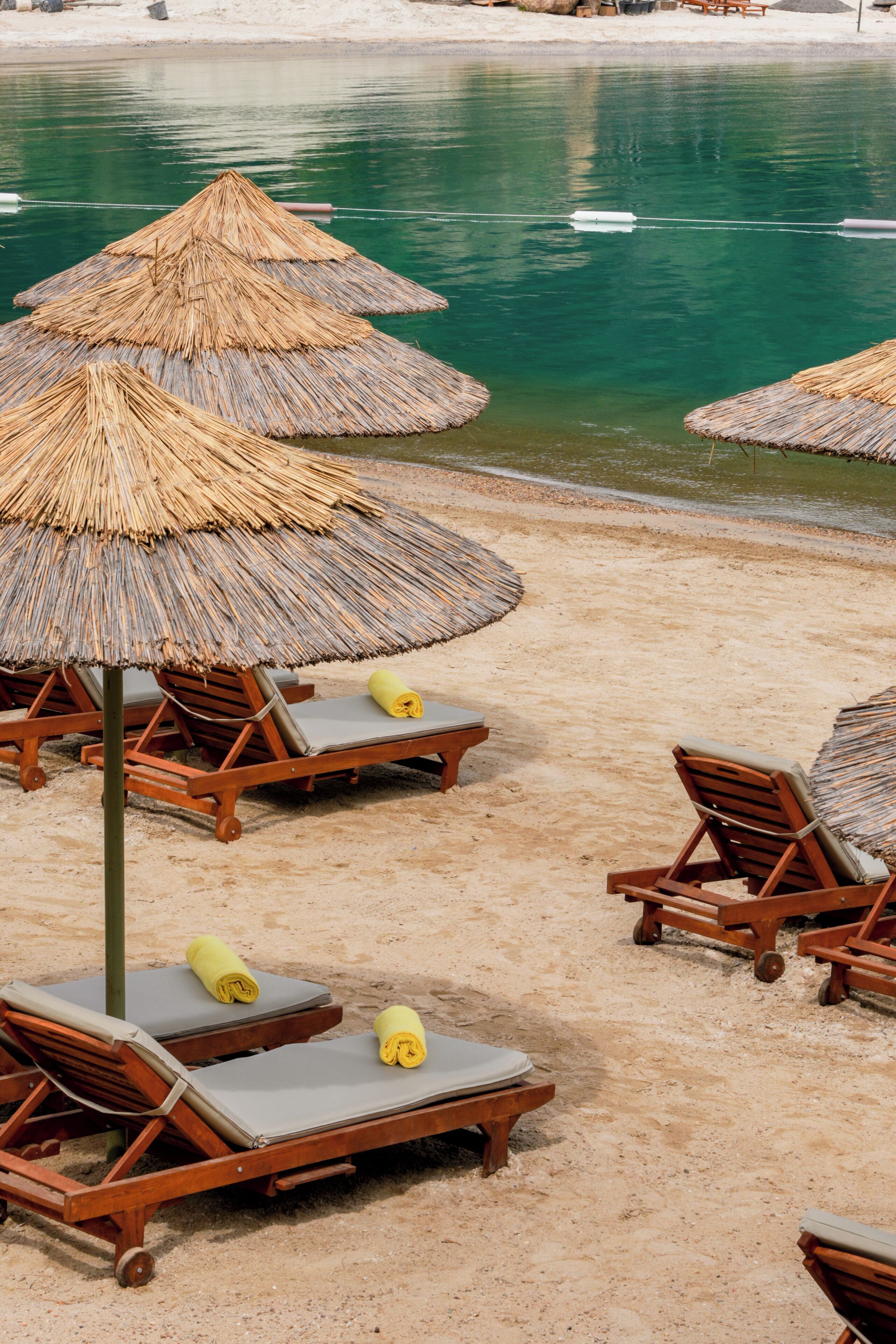 Una playa con sillones de madera y sombrillas de paja.