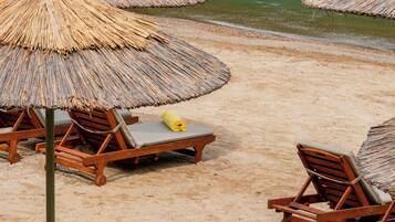 Una playa con sillones de madera y sombrillas de paja.