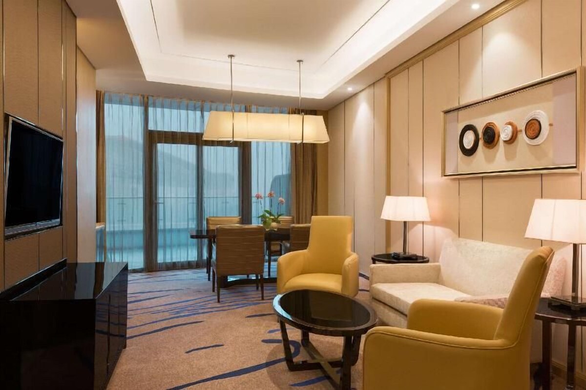 Une chambre d’hôtel équipée d’une télévision, d’un canapé, d’un fauteuil, d’une table à manger et d’une lampe.
