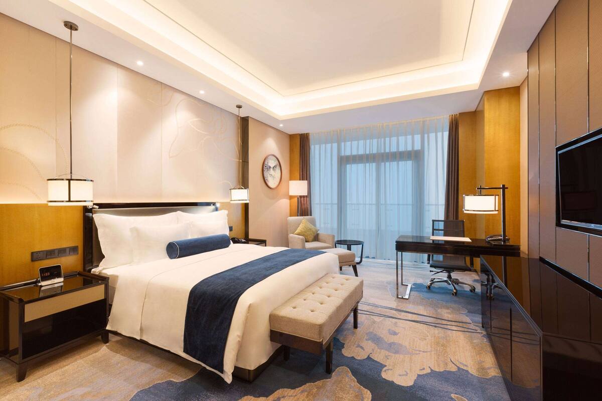 Un cuarto de hotel con una cama grande, un escritorio, televisión y vistas a la ciudad.