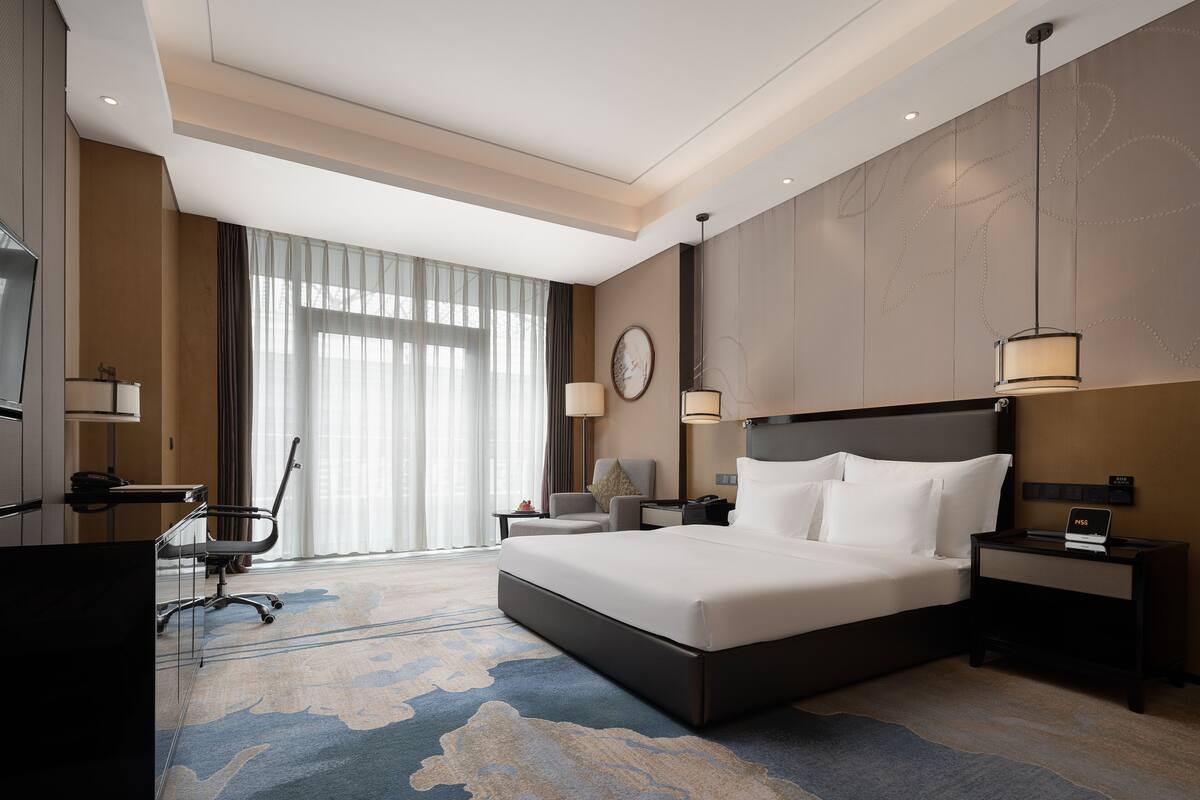 Habitación de hotel con una cama grande, un escritorio, una silla y un televisor.