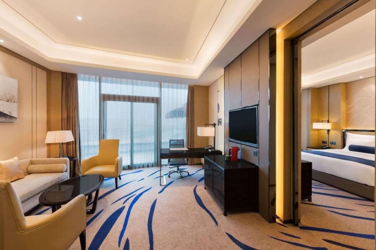 Una habitación de hotel con sofá, sillón, escritorio, televisor y cama.