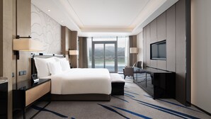 A modern hotel room with a large bed, a desk with a lamp, a TV, and a view of the outdoors. - Wyndham Chongqing Yuelai (Chongqing)