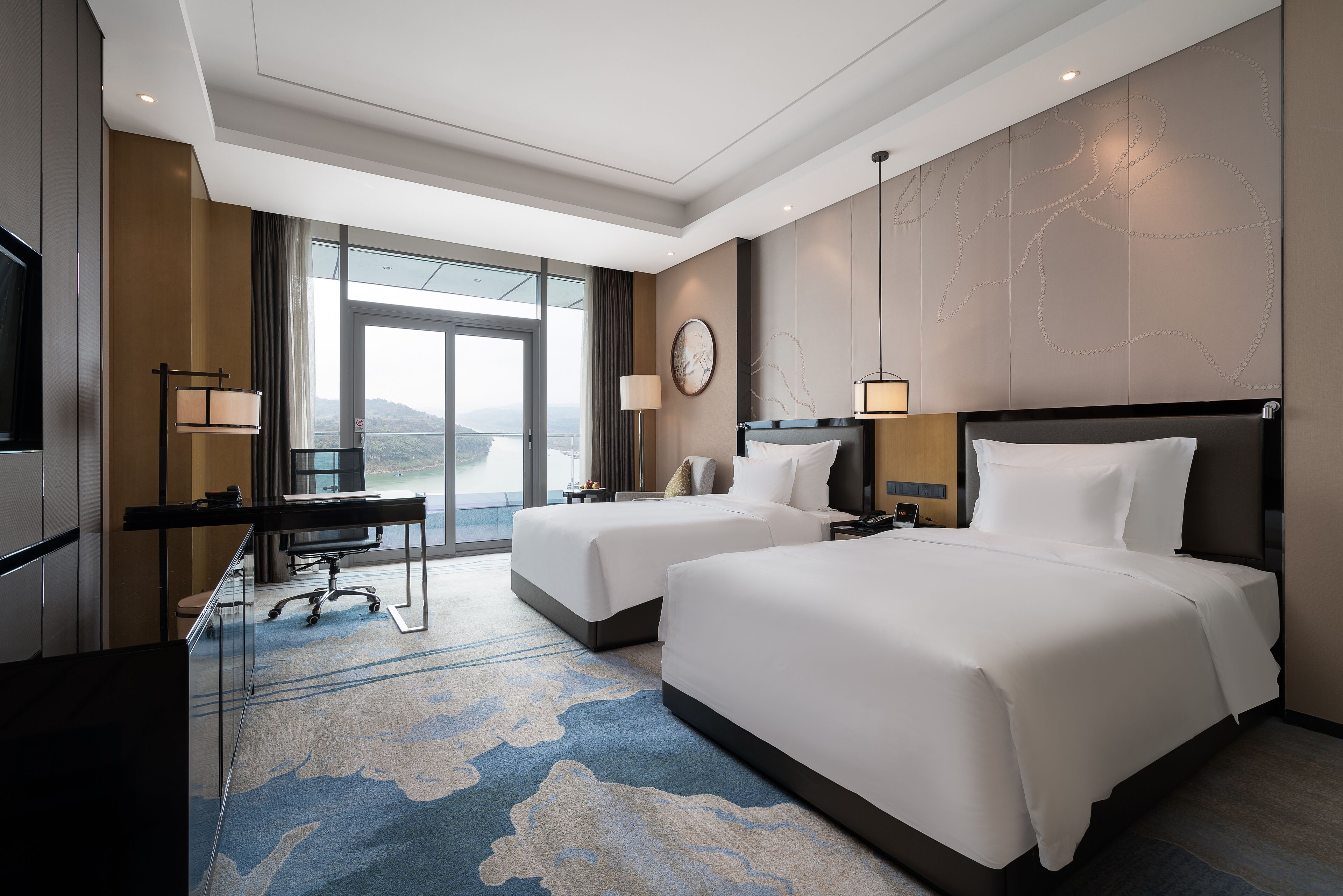 Habitación de hotel con dos camas, un escritorio y un ventanal con vistas al exterior.