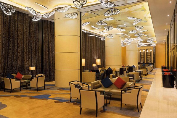 Un hall d’hôtel doté d’un long comptoir d’accueil, de plusieurs espaces de détente avec des fauteuils et des canapés, et d’un tapis à motifs.