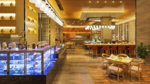 A modern restaurant with a central dining area, a dessert display, and a kitchen in the background. - Wyndham Chongqing Yuelai (Chongqing)