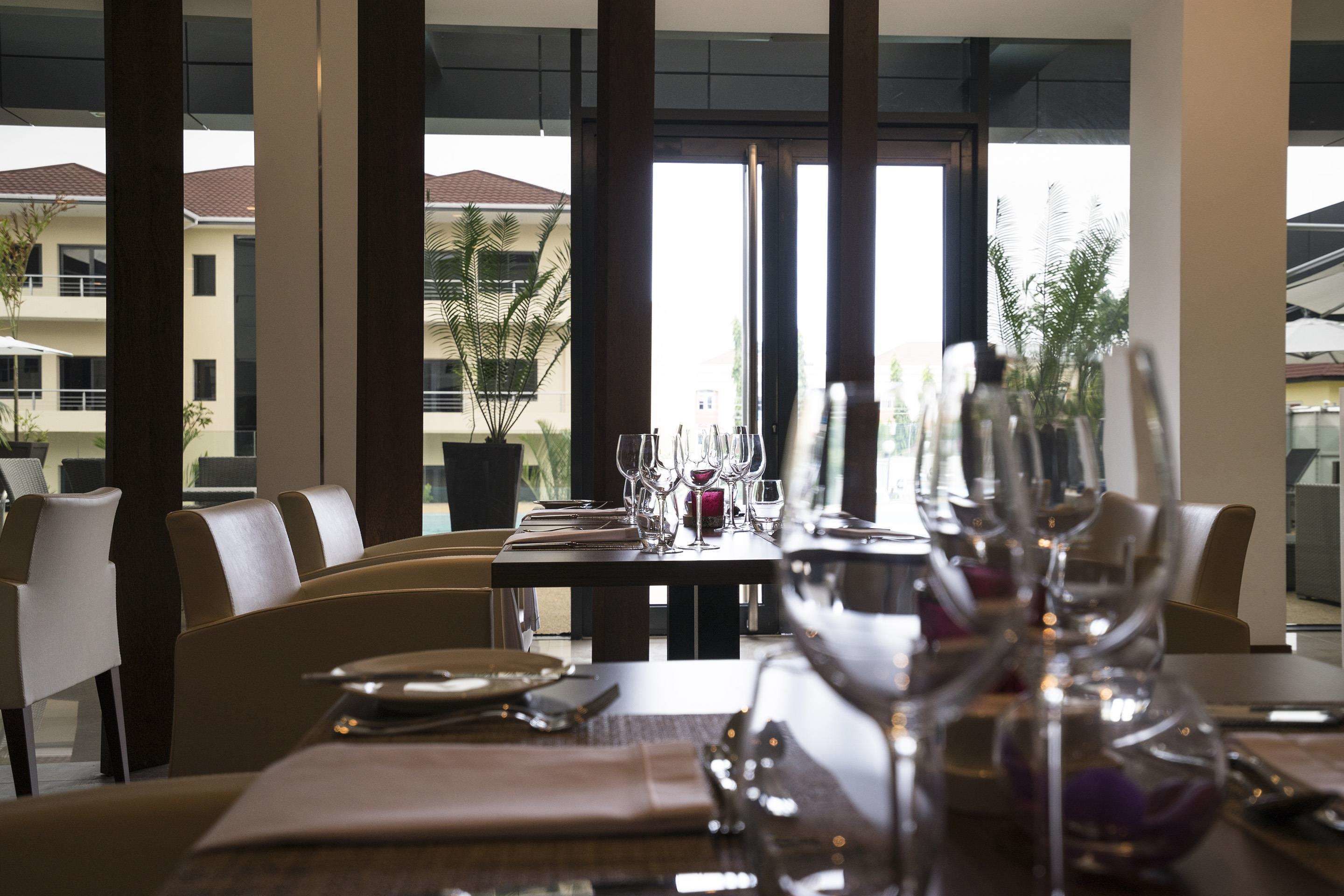 Comedor con una mesa lista para una comida, ventanas amplias y vistas a edificios y árboles.