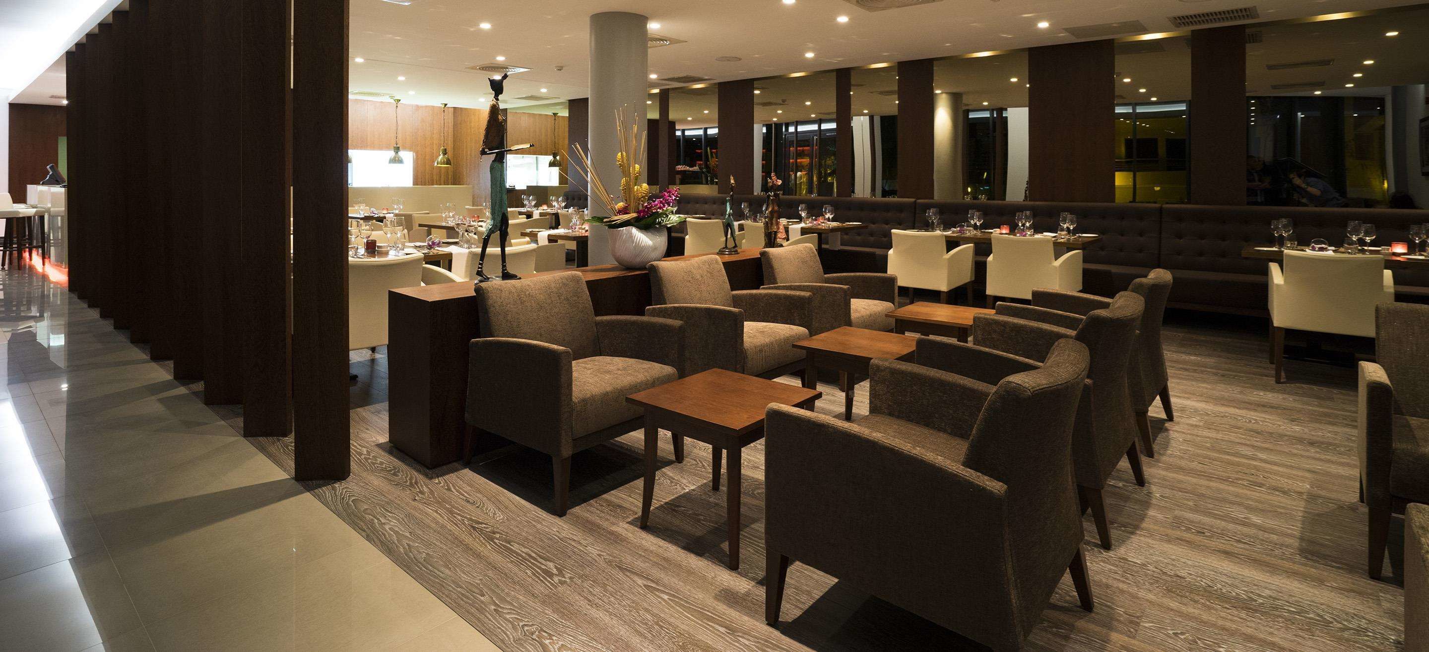 Een moderne hotellobby met verschillende zithoeken, waaronder banken en tafels, en een grote decoratieve vaas met bloemen.